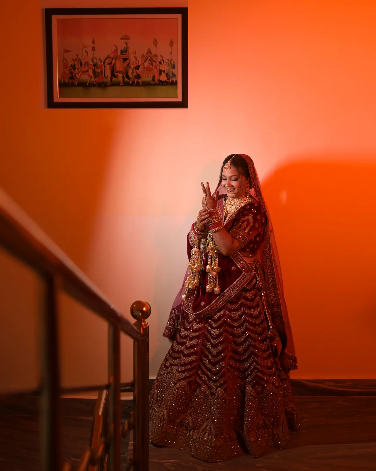 Bride in a deep red lehenga on a staircase against a warm orange wall