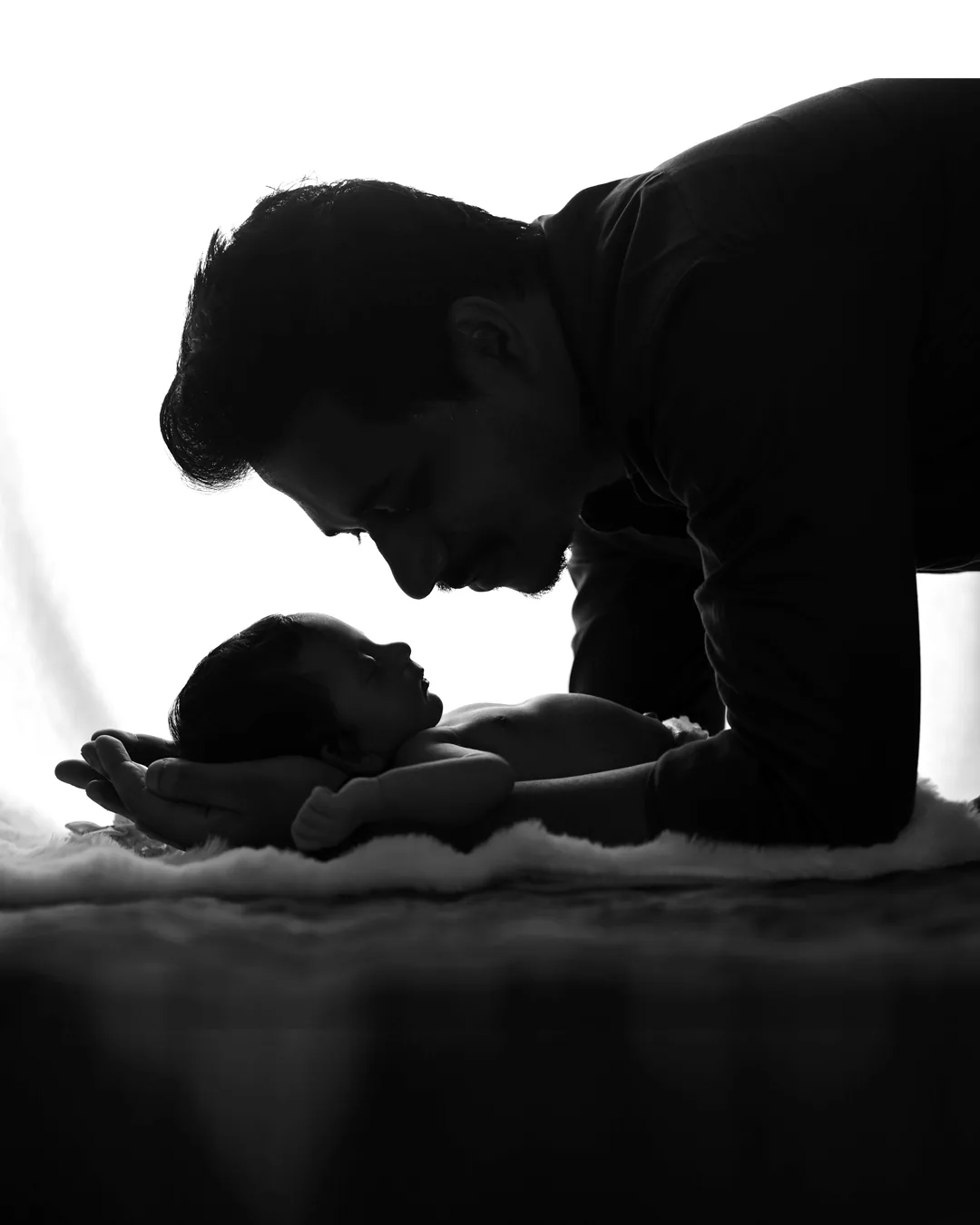 Black-and-white silhouette of a father leaning over his newborn