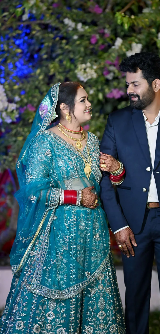Bride in a teal lehenga smiling at the groom in a navy suit