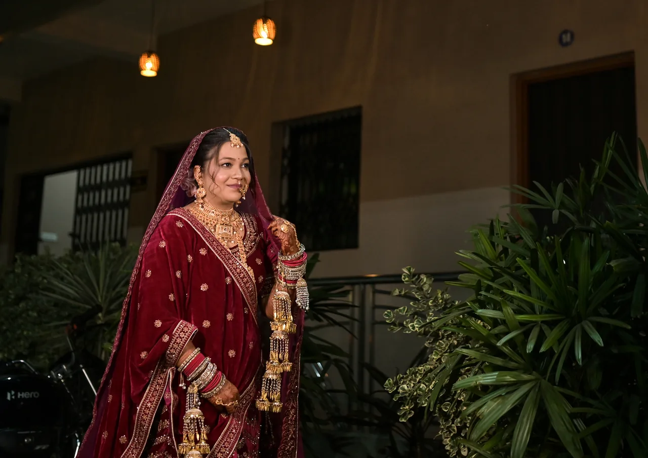 Bride in maroon standing among plants at dusk