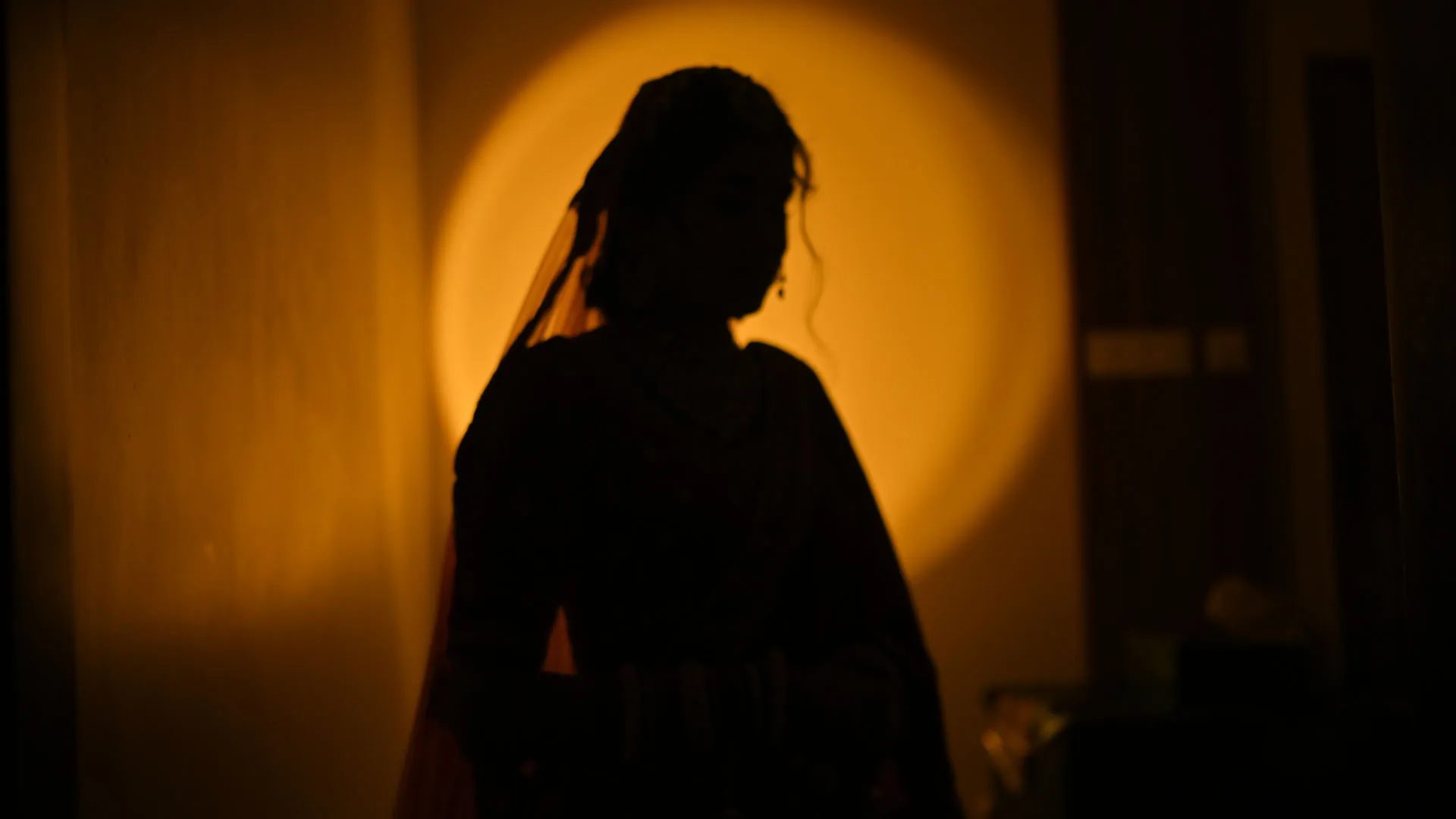 Silhouette of a bride in her veil against a warm golden circle of light