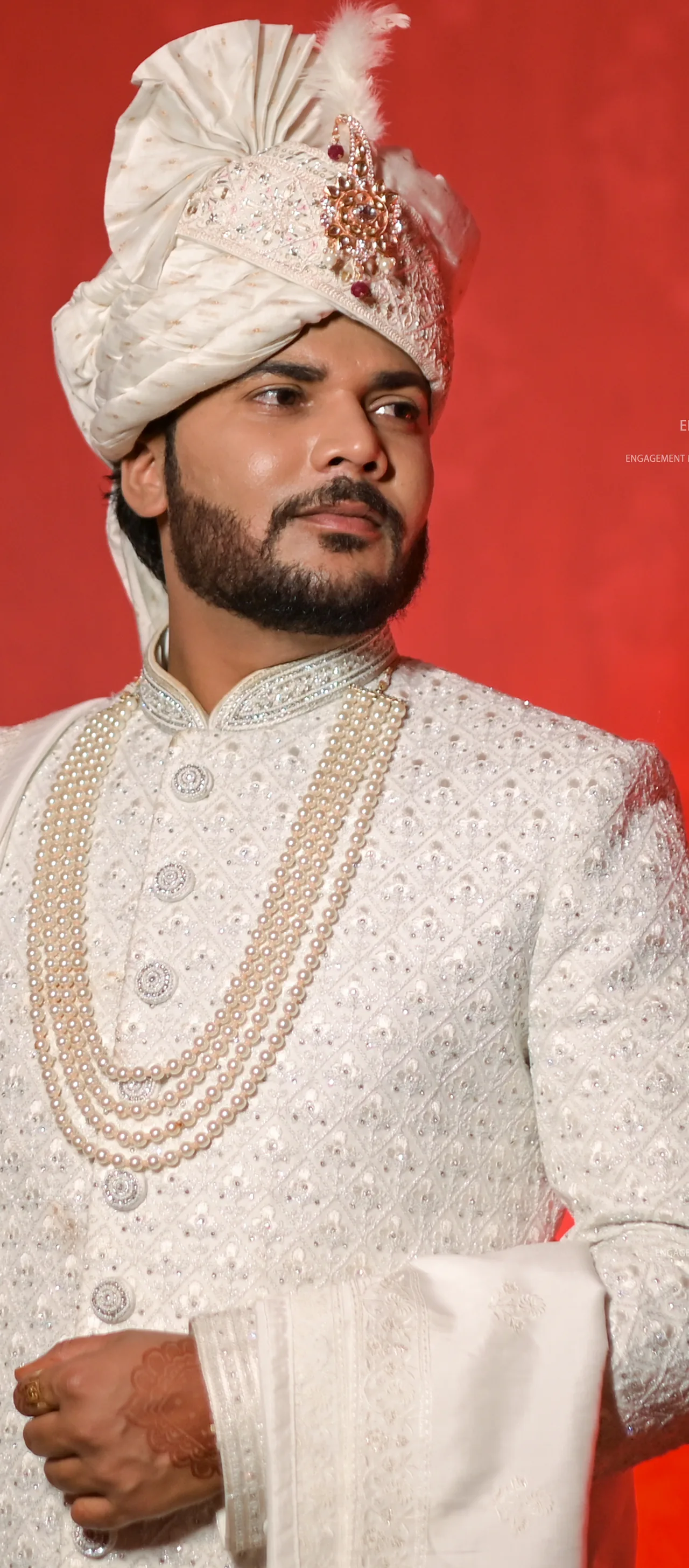 Groom in an ivory sherwani and safa against a red backdrop