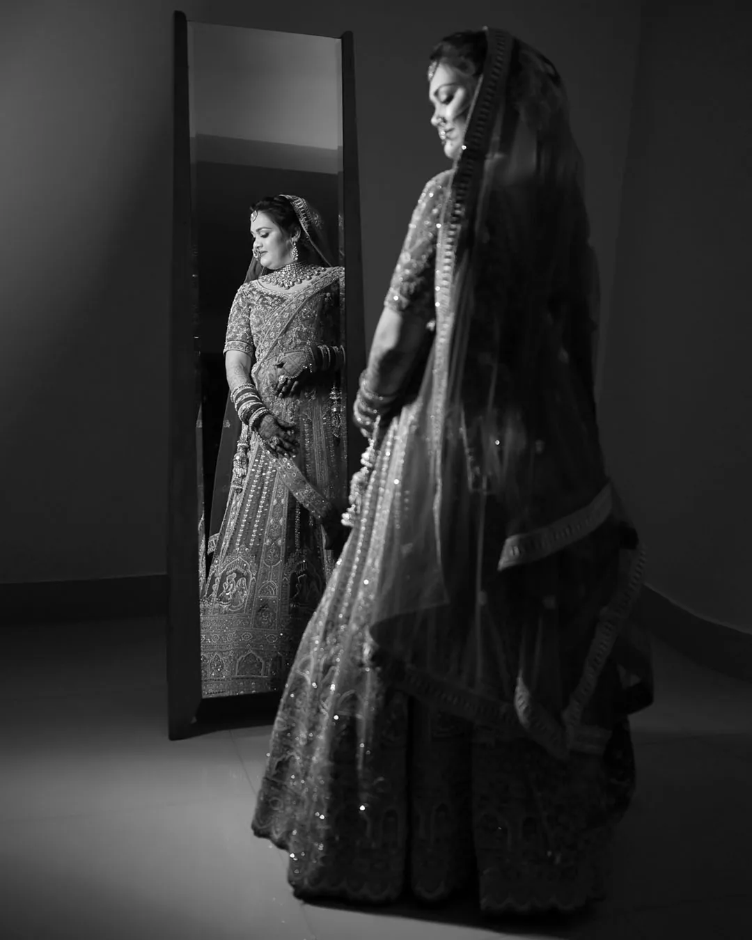 Black-and-white portrait of a bride beside a tall mirror