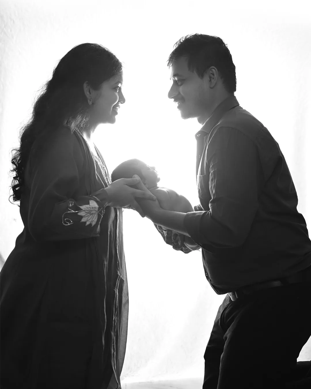 Black-and-white silhouette of parents holding their newborn