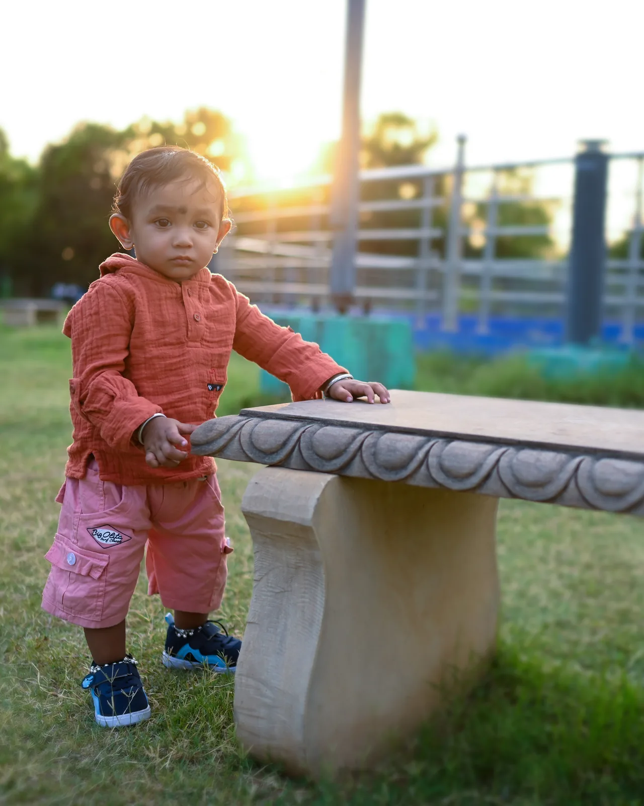 Toddler pushing a stone bench in a park at golden hour