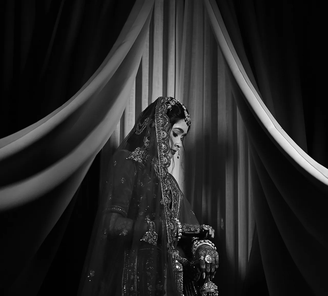 Black-and-white portrait of a bride framed by draped curtains