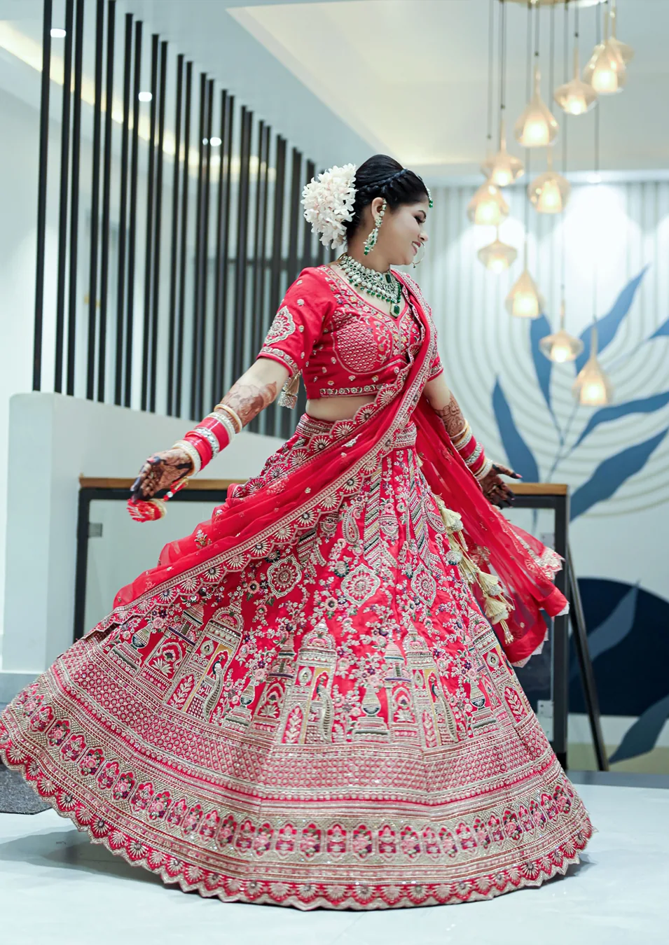 Bride twirling in a red embroidered lehenga beneath hanging lights